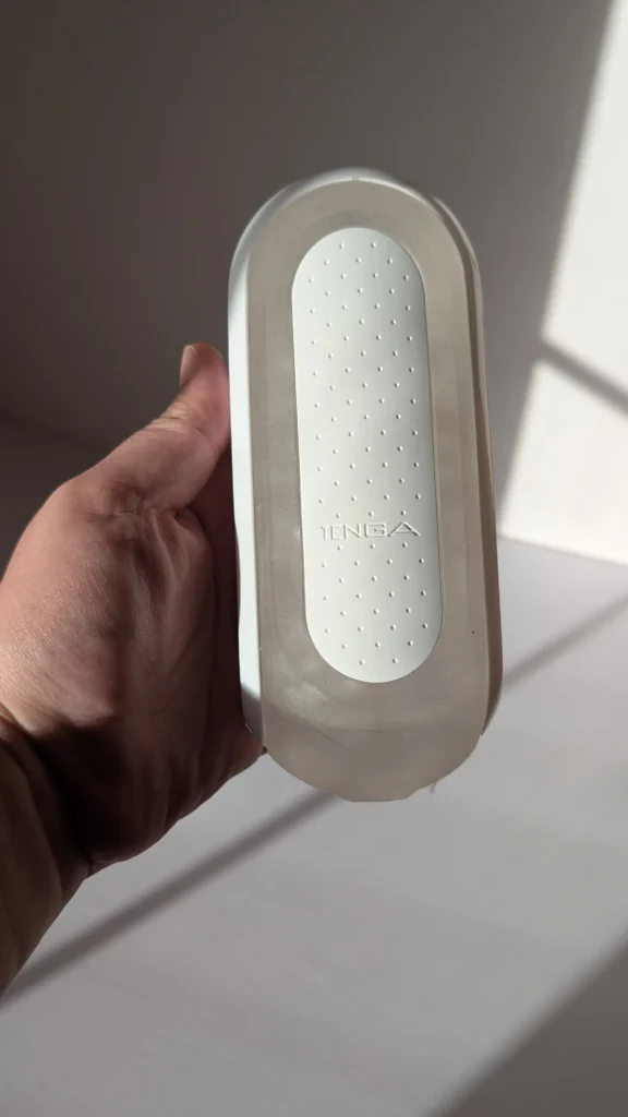 Hand holding the Tenga Flip Zero, showing the dotted white pad inside the clear shell