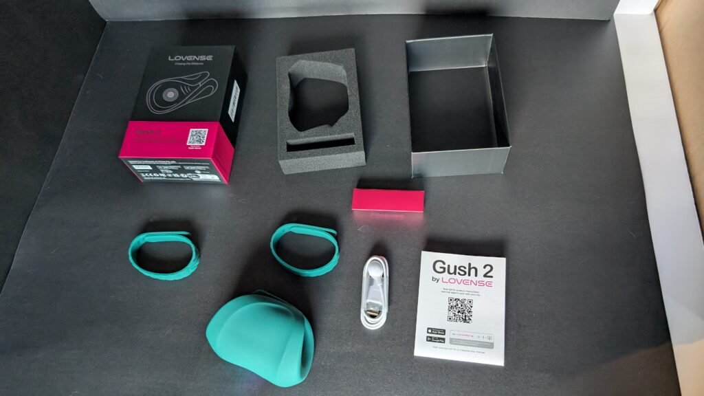 Everything in the Gush 2 box laid out: the teal Gush 2, two adjustable straps, a USB charging cable, a quick-start card and the packaging