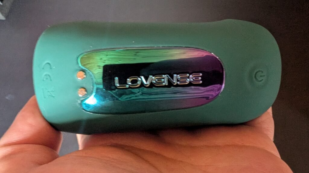 Back of the Gush 2 in hand, showing the iridescent Lovense panel, the magnetic charging contacts and the power button