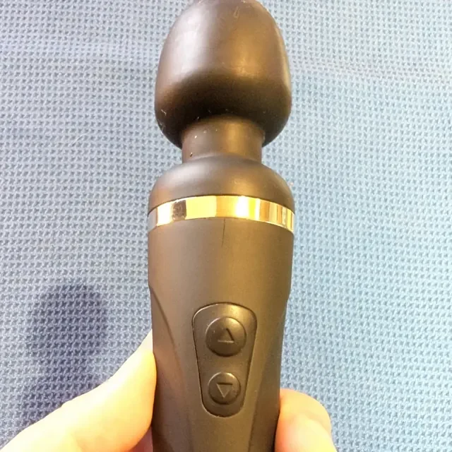 Hand holding the Lovense Domi 2, showing the silicone head, neck, chrome ring and up/down buttons