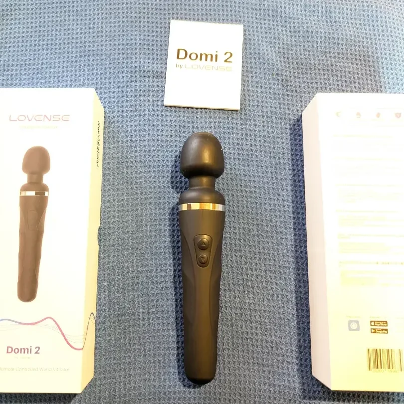 Lovense Domi 2 wand vibrator laid out between the front and back of its retail box, with the Domi 2 manual above
