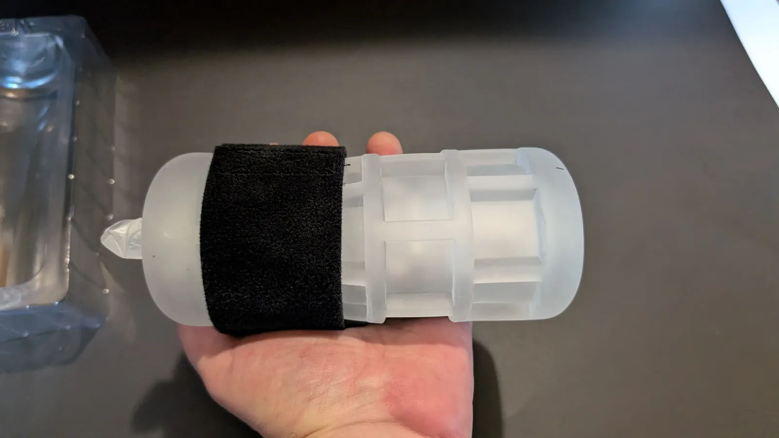 Clear TPE grip sleeve resting in an open hand, its ribbed and windowed outer wall visible beside the black band